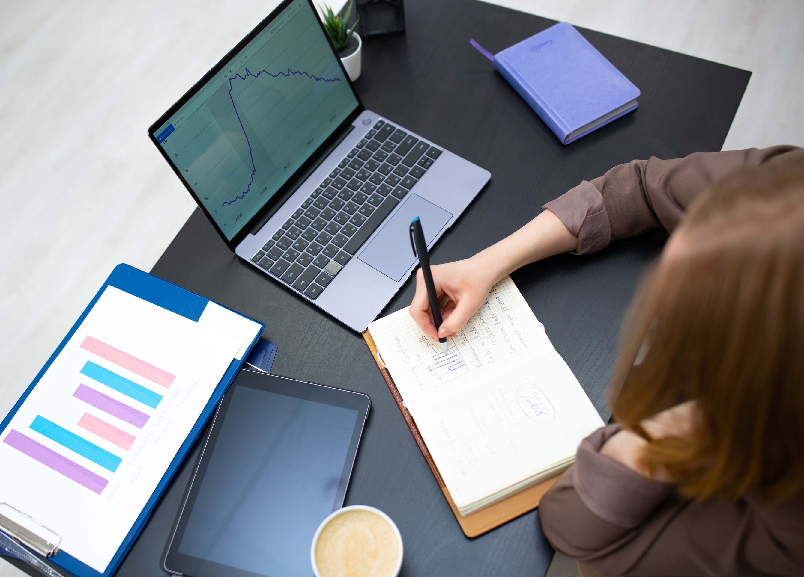 Person schreibt Notizen neben einem Laptop mit Diagrammen im Büro